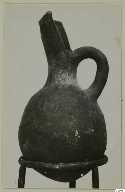 Black-slipped jug with a tall trefoil-type spout and a loop handle, standing on a metal stand