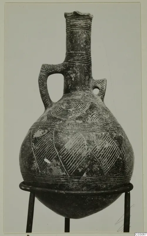 Pottery Red Polished III jug with a tall neck, loop handle and incised decoration, shown on a metal stand