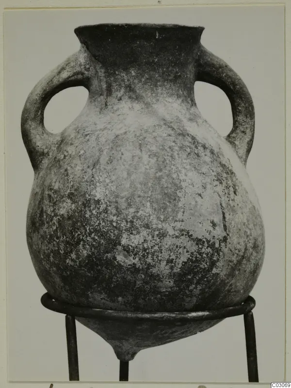 Black Slip Ware amphora with two handles, photographed on a three-legged metal stand