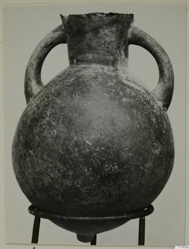 Black-slipped pottery amphora with two loop handles and a wide round body, photographed on a metal stand.