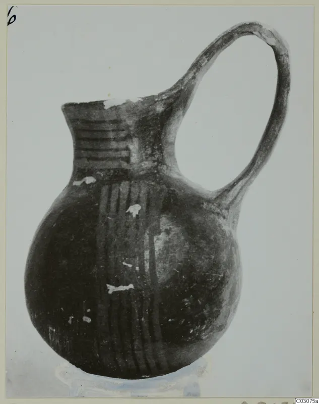 Red-on-black jug with a tall loop handle, photographed against a pale background.