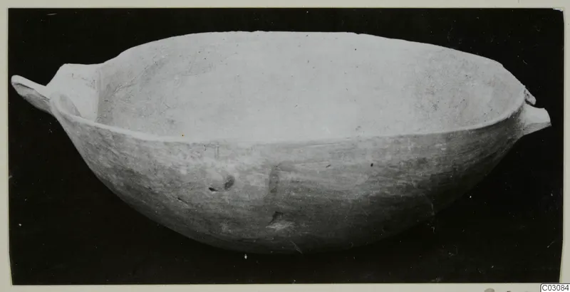 Plain white hand-made bowl with two small handles, photographed against a black background