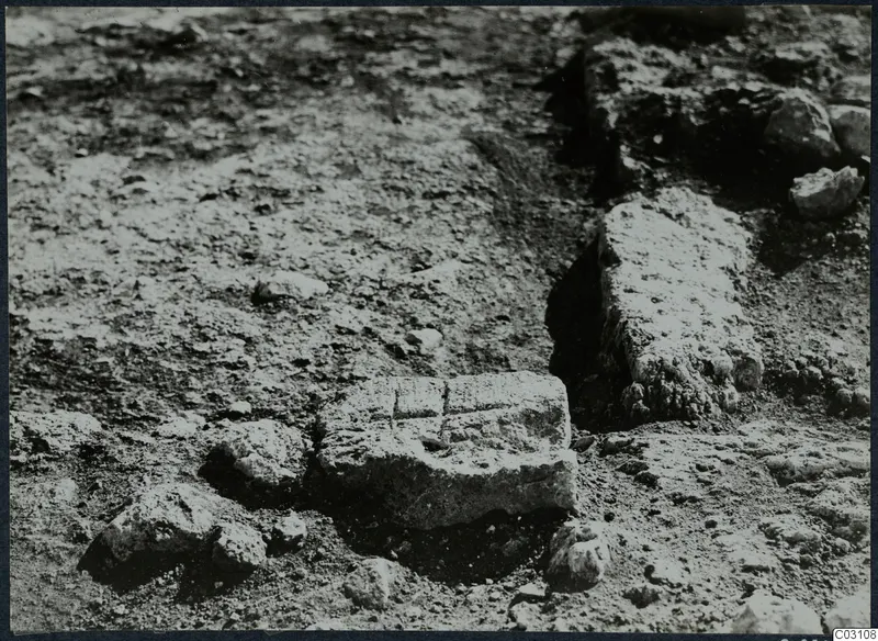 Squared stone block and low stone wall among loose stones in an excavated area at Vouni Palace
