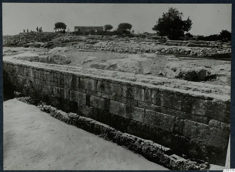 Long wall of large dressed stone blocks at the palace at Vouni, with people and a small building behind