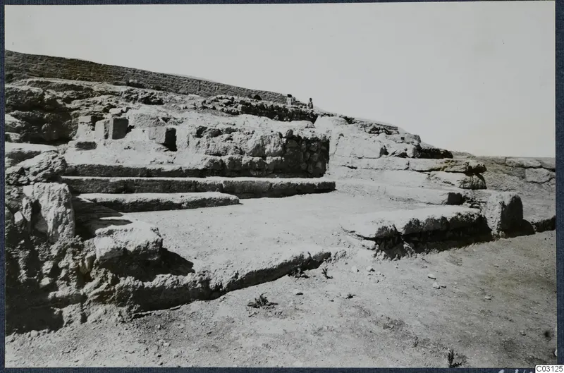 Stone walls and stepped stone ledges at Vouni Palace, with two people standing on the ridge above.