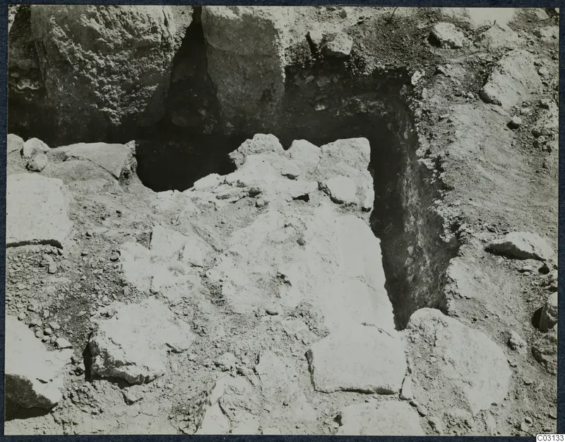 Excavation trench at Vouni with large stone blocks and loose stones lying in excavated soil.