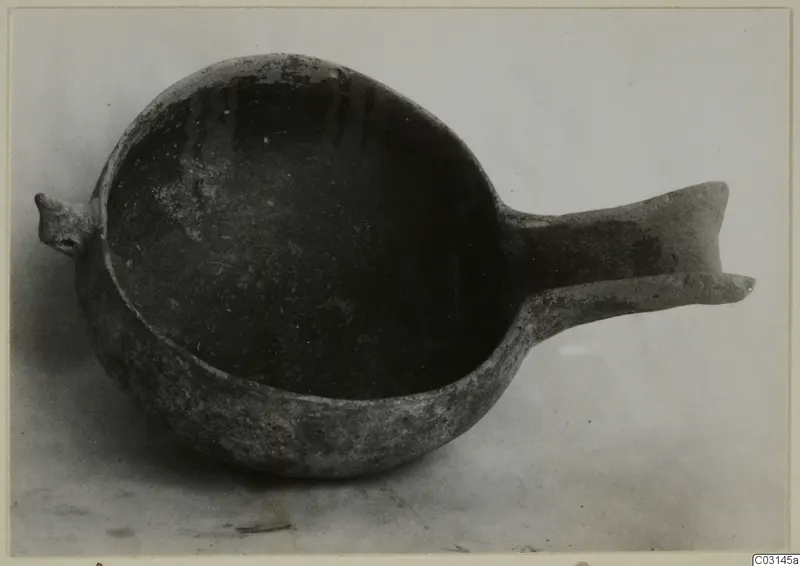 Dark pottery bowl with a long flat handle and a small lug, from Ayios Iakovos