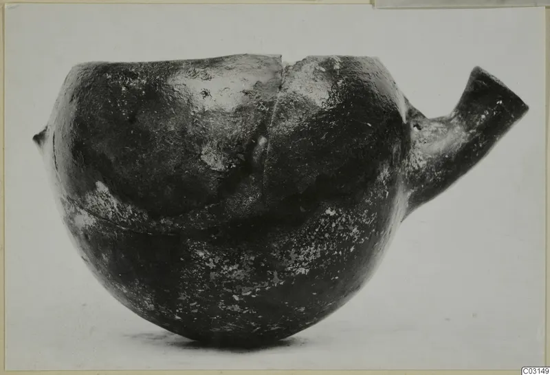 Dark glossy pottery vessel with a tubular spout to the right and a small lug on the left.