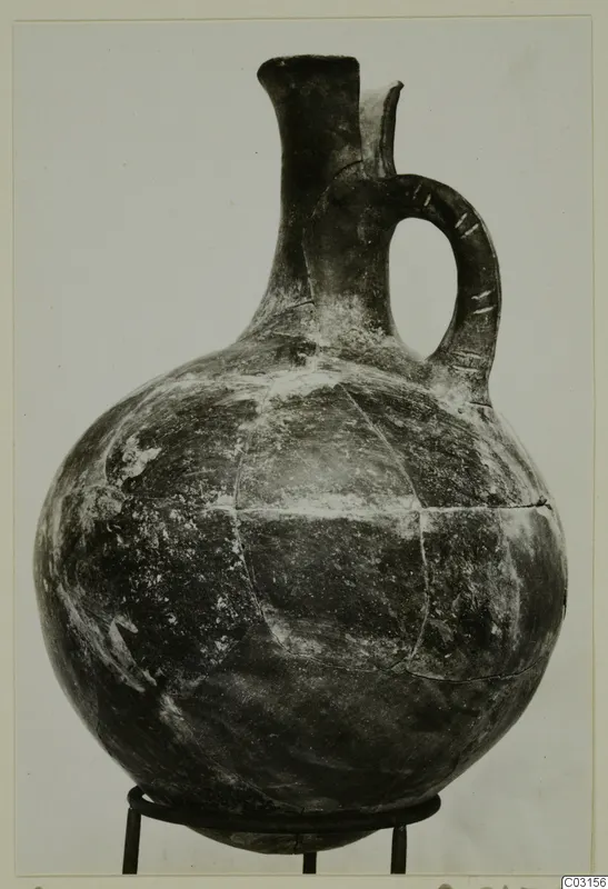 Pottery Red Polished I jug from Lapithos with a strap handle, shown on a three-legged metal stand