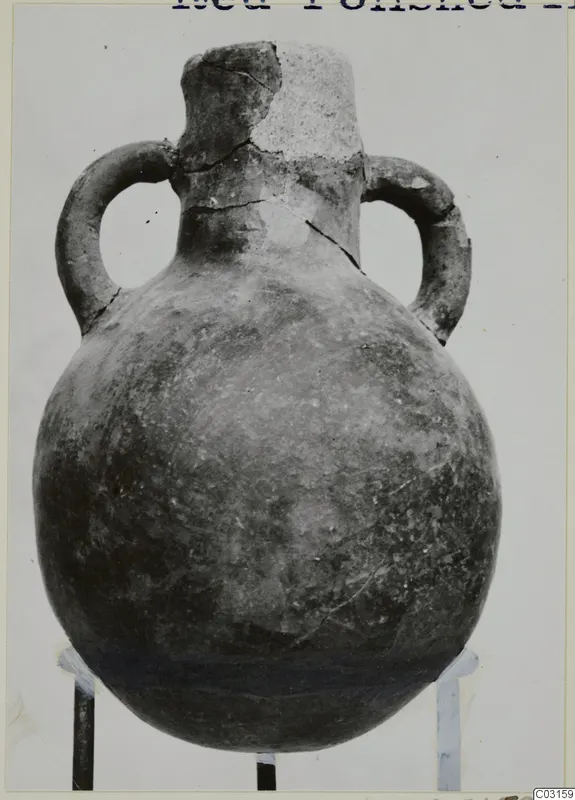 Red Polished III amphora from Lapithos with two loop handles and a broken neck, against a pale background