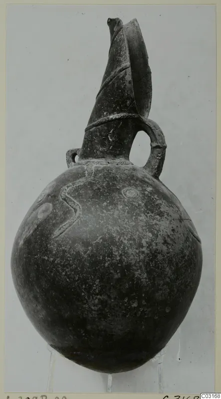 Pottery Red Polished III jug from Lapithos, with a tall flaring spout, loop handle and raised wavy decoration on the body
