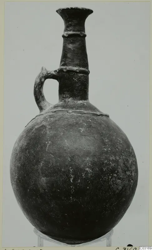 Pottery Red Polished II jug with a flared neck, raised bands and a single loop handle, shown on a stand