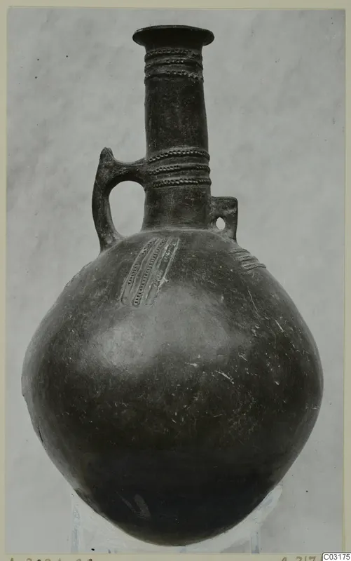 Pottery Red Polished III jug from Lapithos with a long neck, loop handle and impressed dotted bands on neck and body.