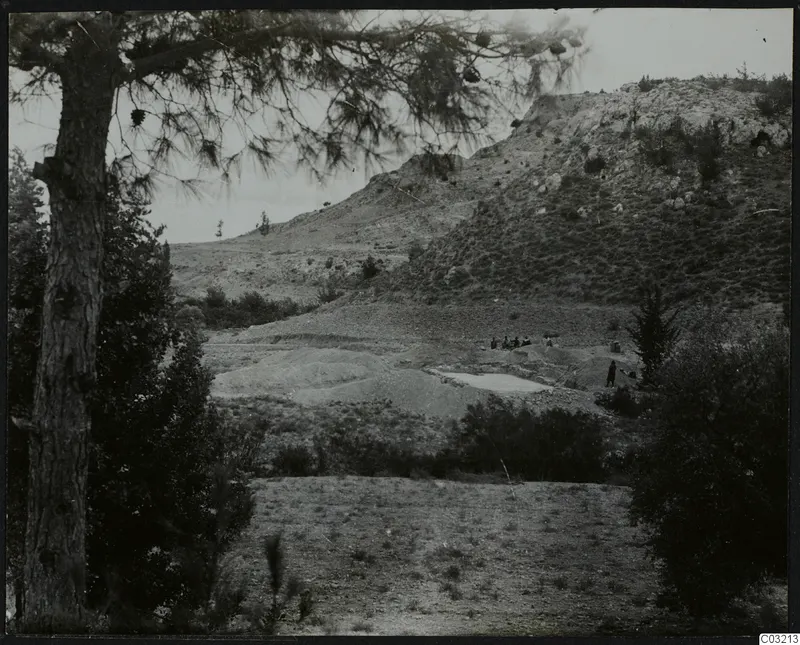 Mountain landscape at Ayios Iakovos with a pine tree in the foreground, a rocky hill, spoil heaps and a small group of people