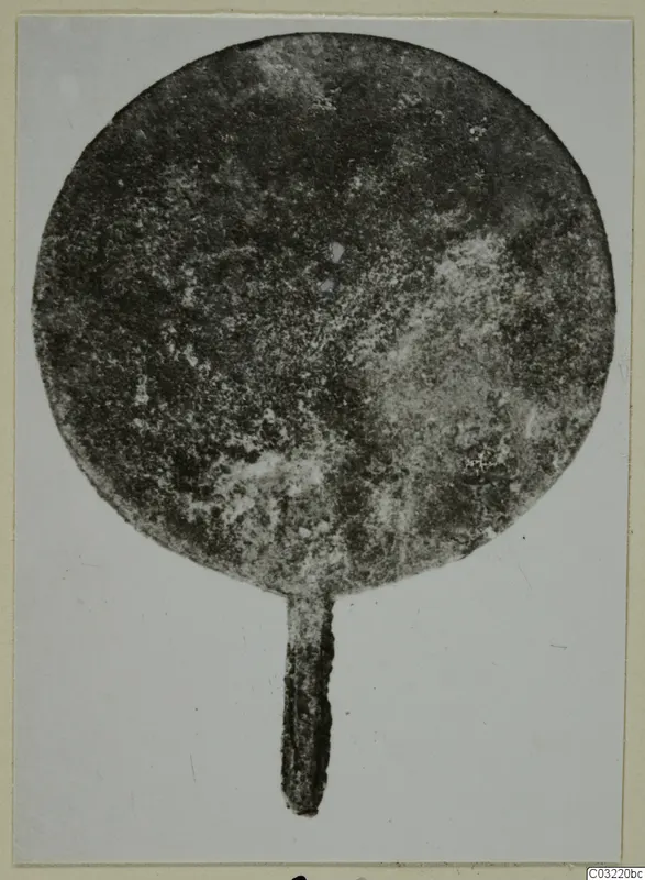 Corroded round metal disc with a narrow tang at the bottom, from Marion