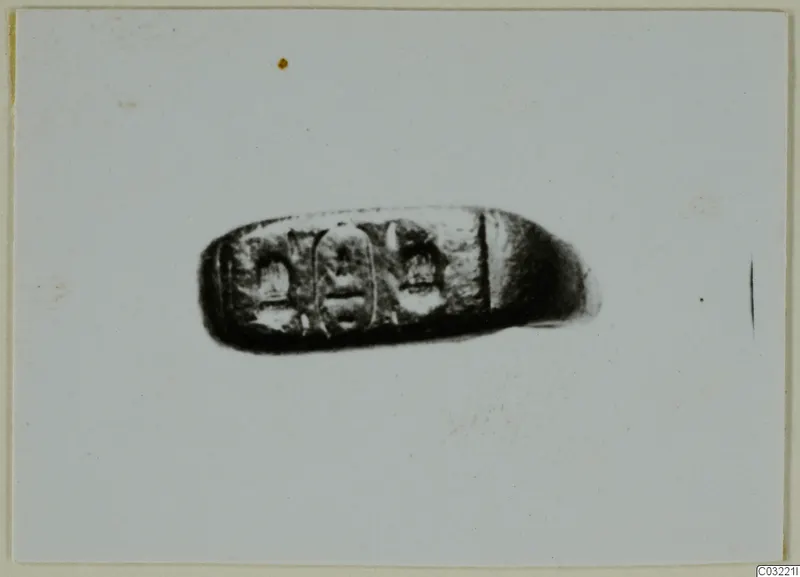 Dark oblong object with three engraved panels, possibly a ring bezel or seal