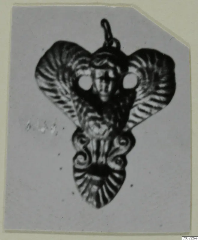 Pendant with a loop at the top, a central face between two round openings, and flaring side lobes with ridged surfaces