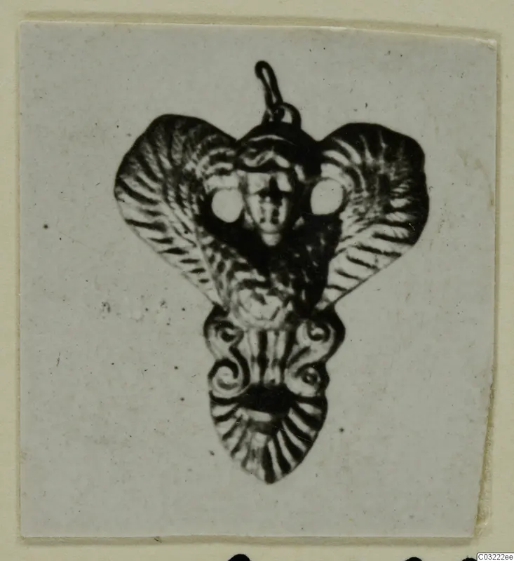 Ornamental pendant with a loop at the top, a small face at the centre and fan-shaped flaps, from Marion Tomb 60