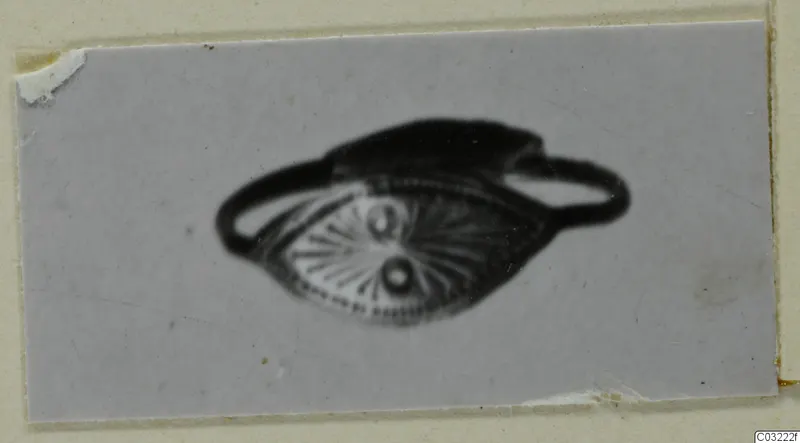 Ring with an oval bezel decorated with radiating lines and two dots, shown on a grey card mount