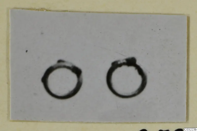 Two bronze personal adornments, plain ring-shaped objects, photographed side by side on a pale grey background