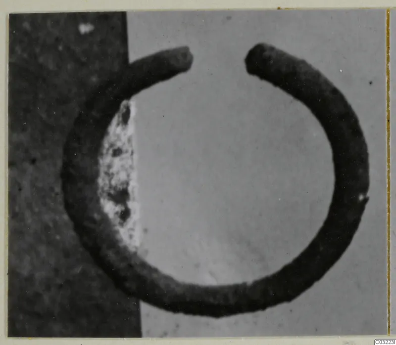 Open bracelet of dark metal, a thick band with two ends that do not meet, photographed on a grey ground