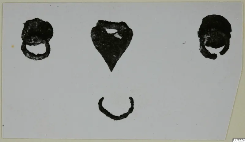 Four bronze mounting fragments on a pale card: two rounded loop pieces, a pointed plate and a small arc.