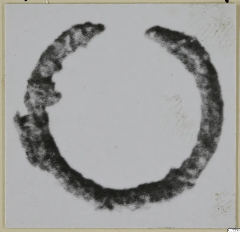 Open bronze ring with a dark, mottled surface, photographed against a pale background