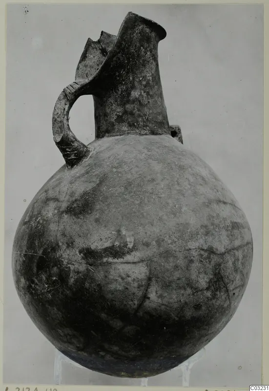 Red Polished III jug from the Vrysi tou Barba tombs at Lapithos, shown on a stand against a plain backdrop