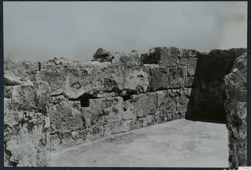 Stone wall of large squared blocks at the palace at Vouni, with a dark opening to the right.
