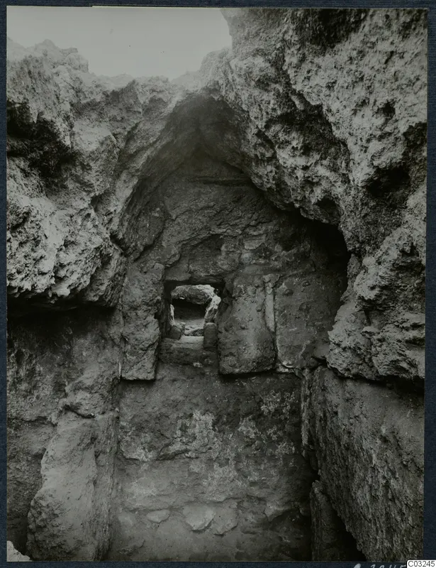 Narrow excavated cutting at Vouni palace, with rough rock walls and a stone-framed doorway opening onto a second passage