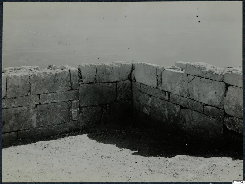 Corner of a stone wall of large rectangular blocks at the palace at Vouni, on a bare ground surface.