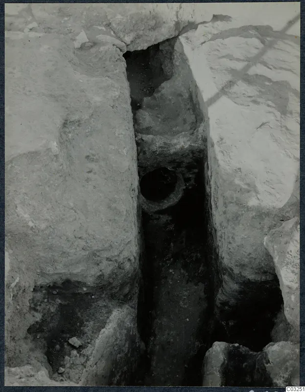 Narrow excavated trench between large stone blocks at the palace at Vouni, with a round opening set into one side