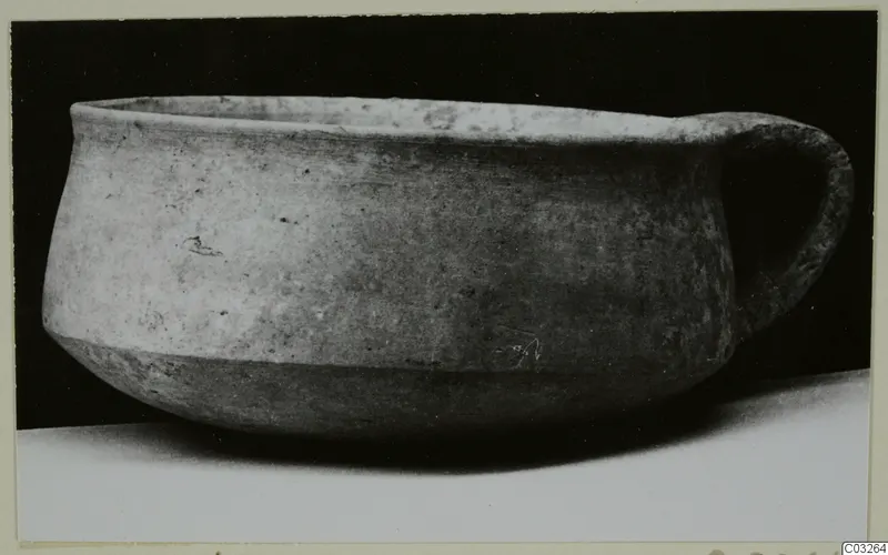 Plain white wheel-made pottery bowl with a single loop handle, from Milia