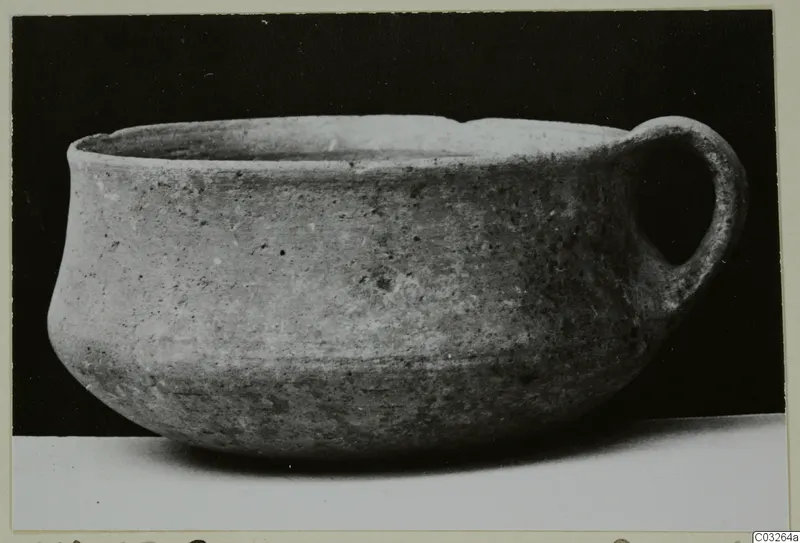 Plain pottery bowl with a single loop handle on the right, photographed against a black background.