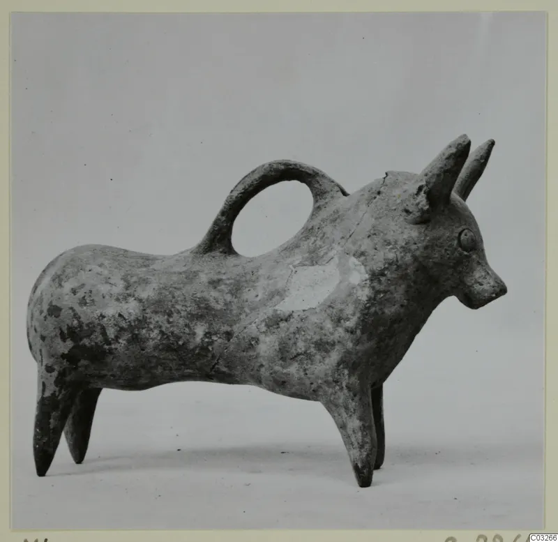 Bull-shaped pottery vessel with a loop handle over its back, in Base-Ring Ware, photographed against a grey backdrop