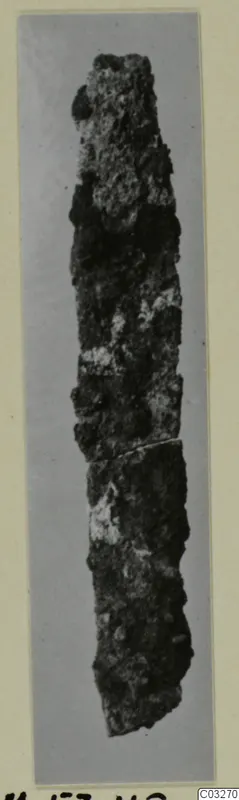 Corroded iron tool, long and narrow, shown upright on a grey background