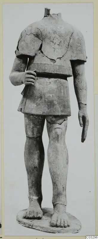 Headless terracotta statue of a standing figure in a short belted garment, on an oval base