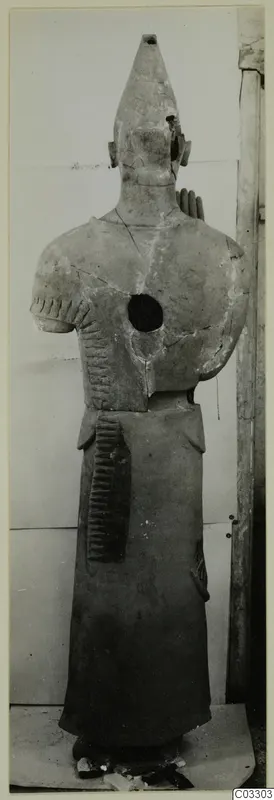 Terracotta statue of a standing figure with a tall conical headdress and comb-like incised marks on arms and skirt
