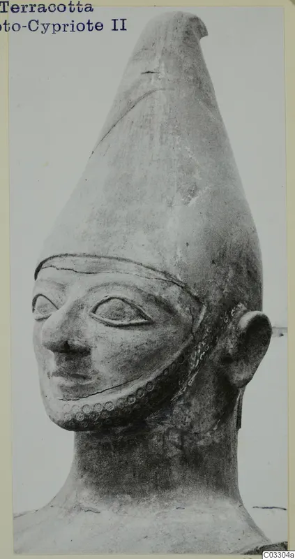 Terracotta head with a tall conical headdress, almond-shaped eyes and a row of round impressions along the jaw