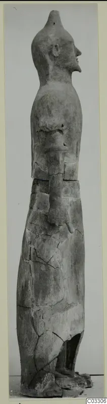 Tall terracotta statue of a standing figure in side profile, with a pointed head and cracked surface
