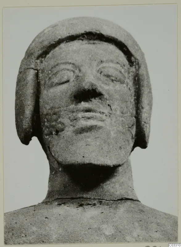 Frontal view of a terracotta statue head with incised eyes, nose and mouth, and a band over the hair.