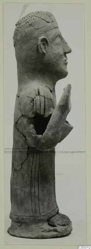 Side view of a grey terracotta standing figure with raised hands, cracked and partly broken.