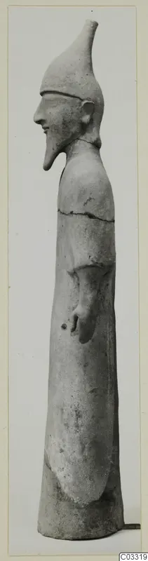 Side view of a pale clay standing figure with a tall conical headdress and pointed beard, from Ayia Irini