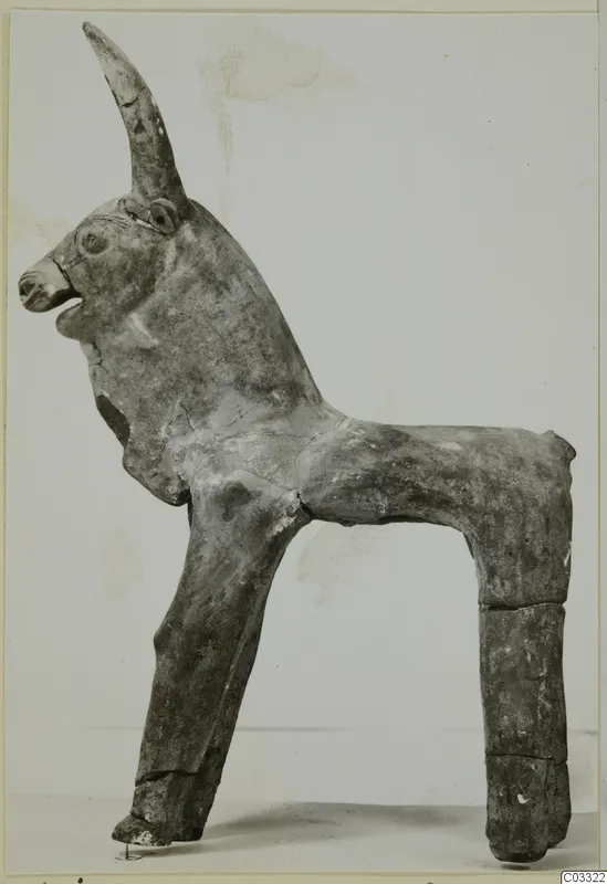 Terracotta figurine of a horned animal, standing, shown in side view against a plain background
