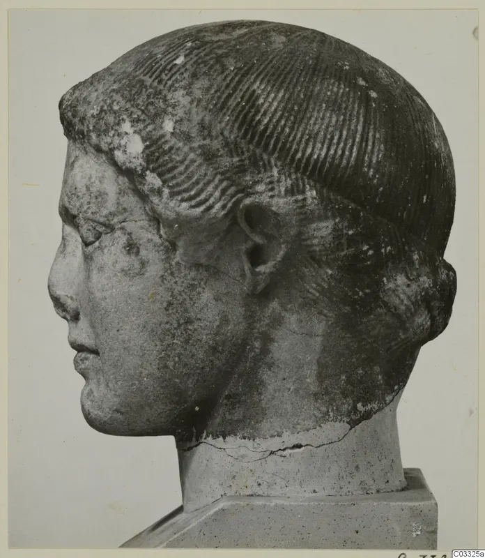 Carved stone head of a figure in profile facing left, with rows of incised hair, on a square base.