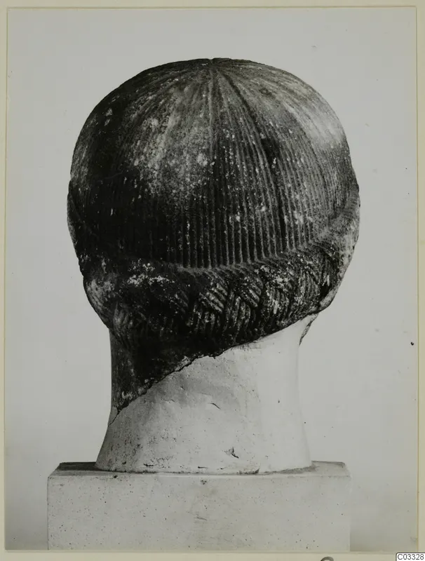 Back view of a carved stone head with grooved hair and a braided band, set on a pale neck support and plinth