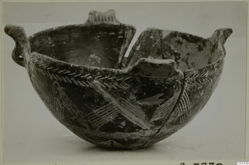 Broken pottery bowl with two upright handles and a dark body decorated with pale chevron and herringbone bands.