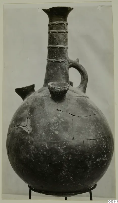 Red Polished II jug with a tall neck, ring-studded collar bands, a side spout and a loop handle, on a metal stand