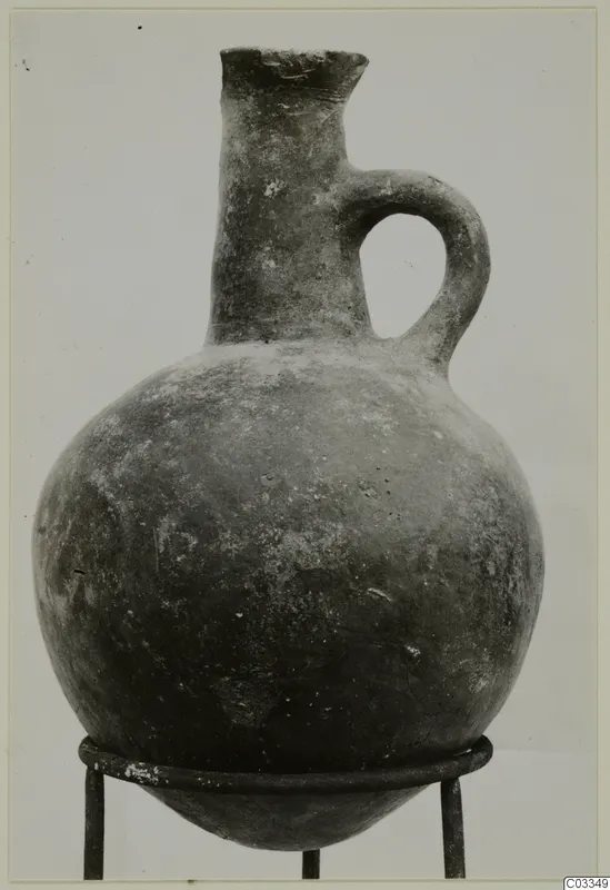Pottery Red Polished II jug with a single loop handle, shown on a metal stand against a plain background.