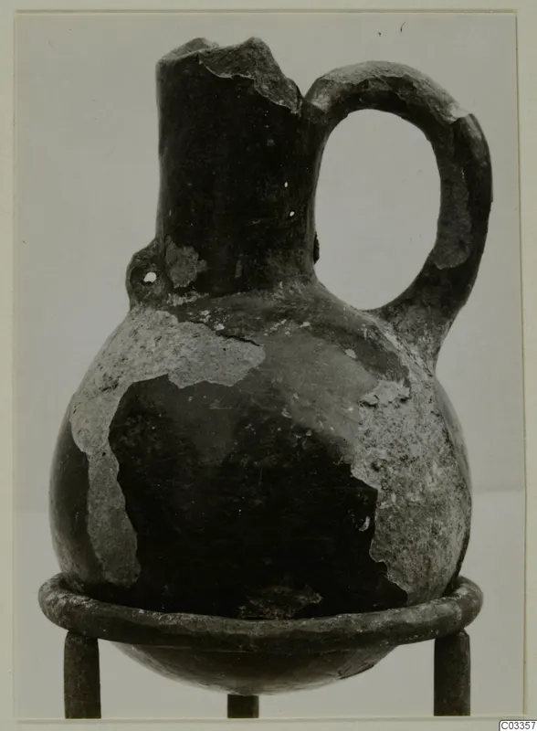 Red Polished III jug from Lapithos, with a single loop handle and broken rim, standing on a metal ring stand